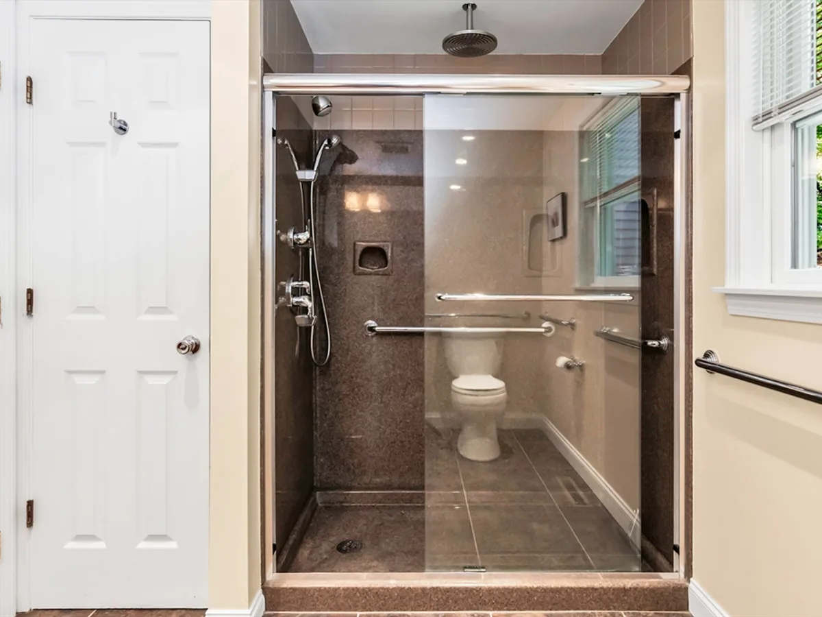 Bathroom with walk-in shower, grab bars, and nearby entry door